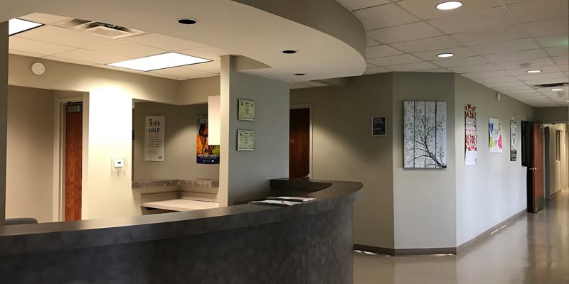 A clean, modern reception area with a curved desk and soft lighting, leading to a hallway decorated with colorful artwork, creating a professional and welcoming space.