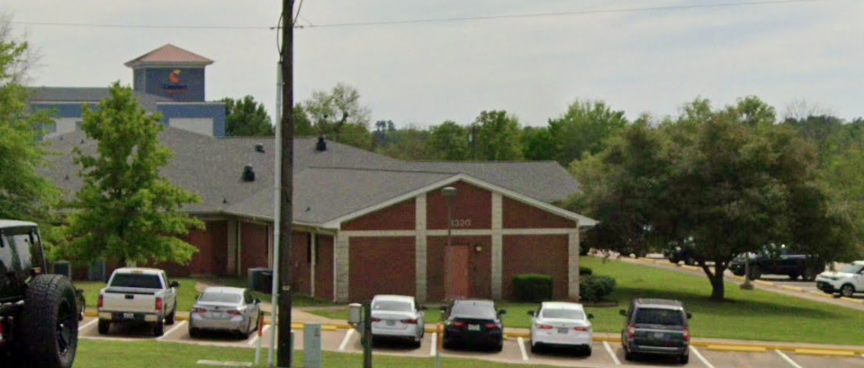 Brick facility with parking lot and trees in front