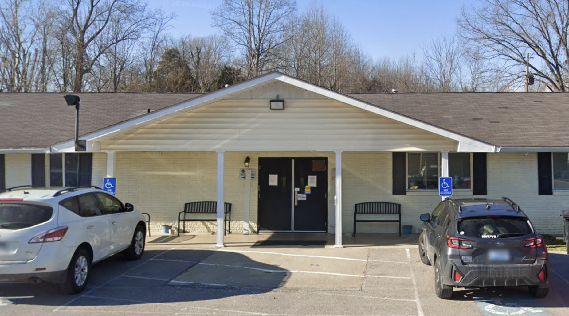 Covered entrance with double doors, benches, and parking spaces