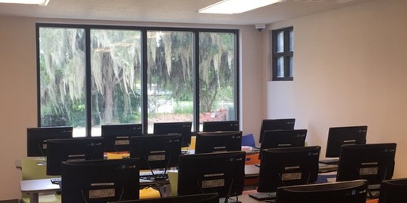 Modern computer lab with large windows offering a peaceful view of trees, providing a comfortable and focused learning environment.