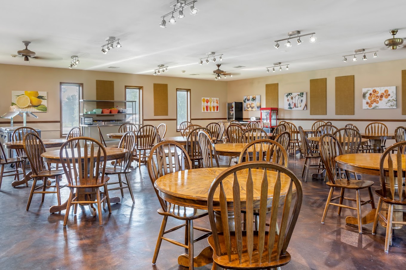 A cozy dining hall with multiple round wooden tables and chairs, decorated with warm lighting and food service stations.