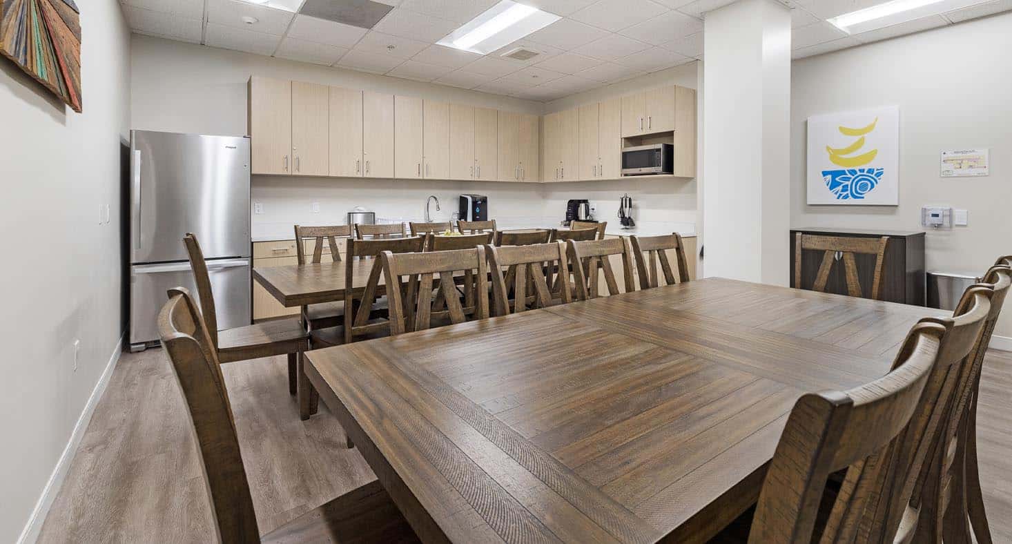 Bright kitchen with long wooden dining tables and stainless fridge.
