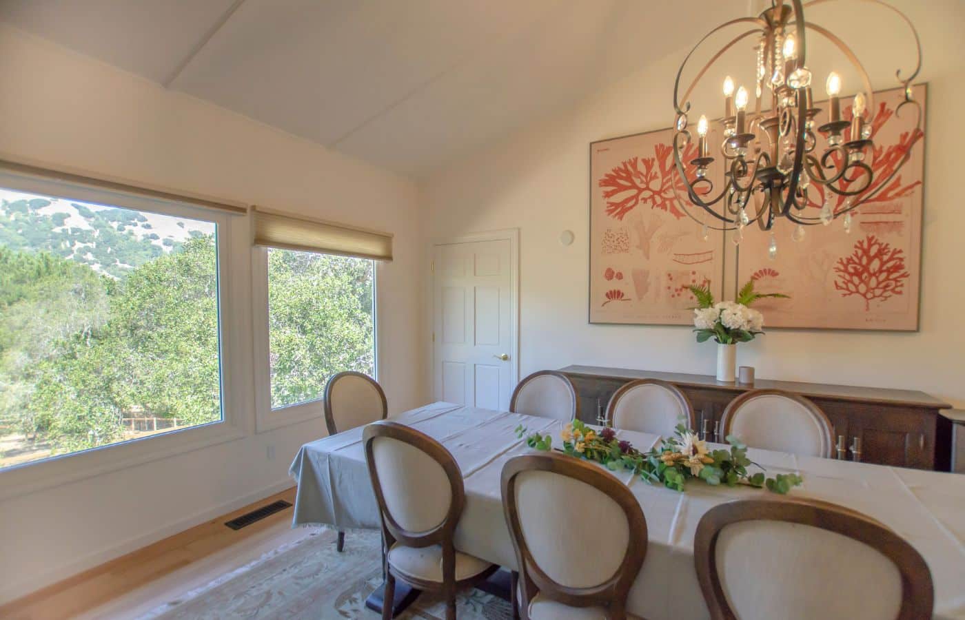Dining room with chandelier and table set beside large windows.