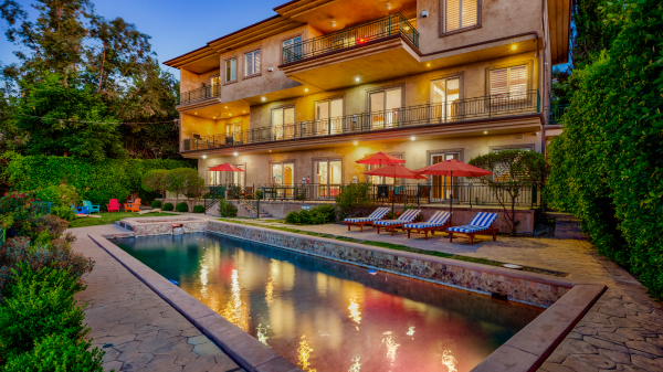Evening view of pool area with lounge chairs, red umbrellas, and three-story building exterior