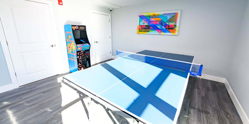 Bright recreation room with a ping pong table, classic arcade game, and colorful wall art, creating a fun and lively environment for relaxation.