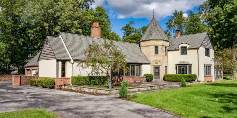 Charming estate with unique architecture, including a turret and gabled roofs, surrounded by lush greenery and a peaceful setting.