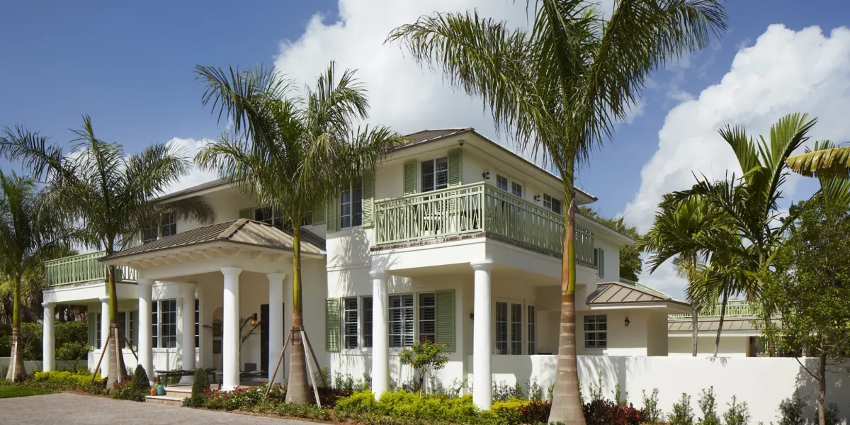White two-story building with green shutters and palms