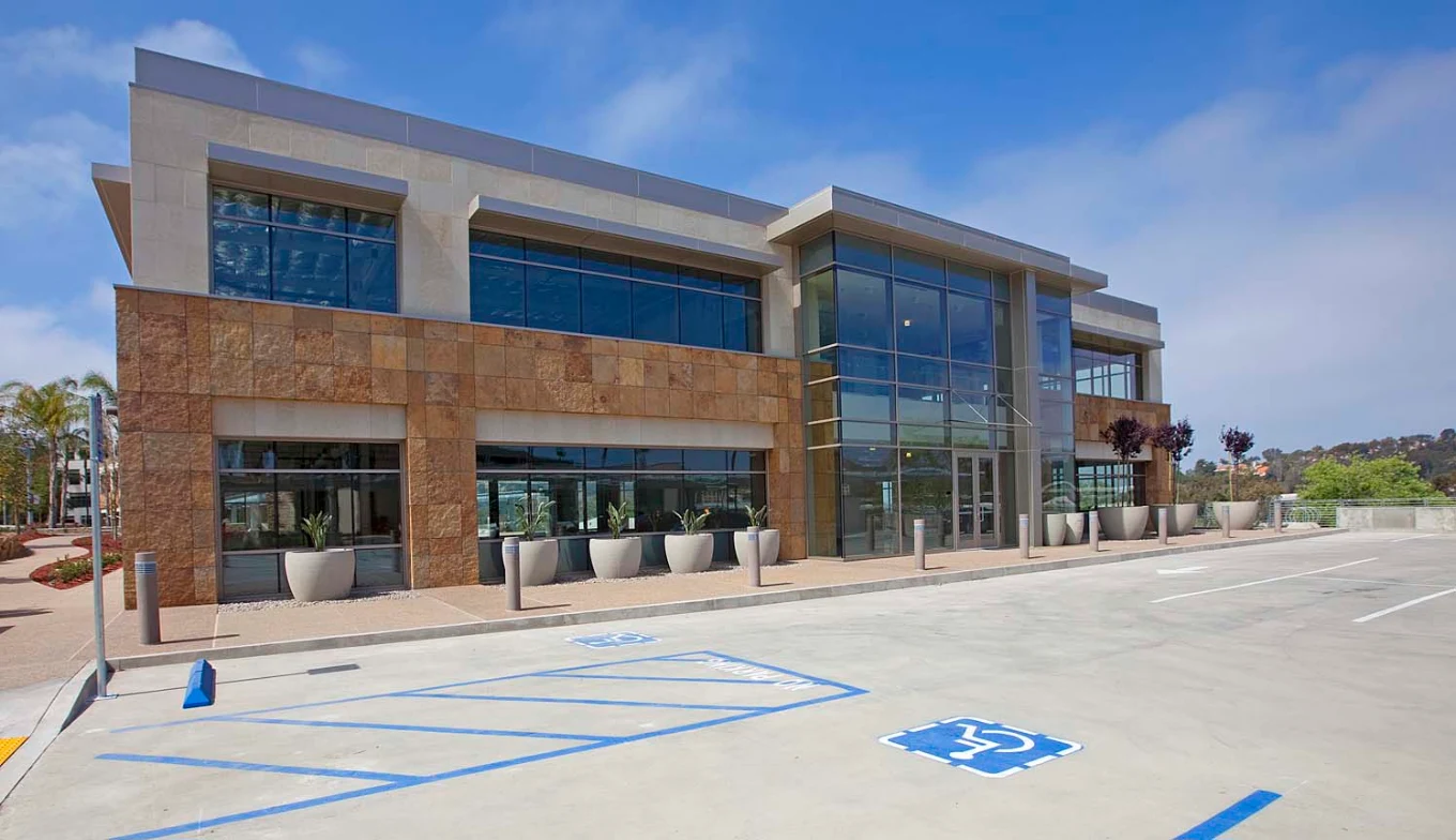 Modern Betty Ford Center building entrance with large glass windows, stone facade, planters, and accessible parking