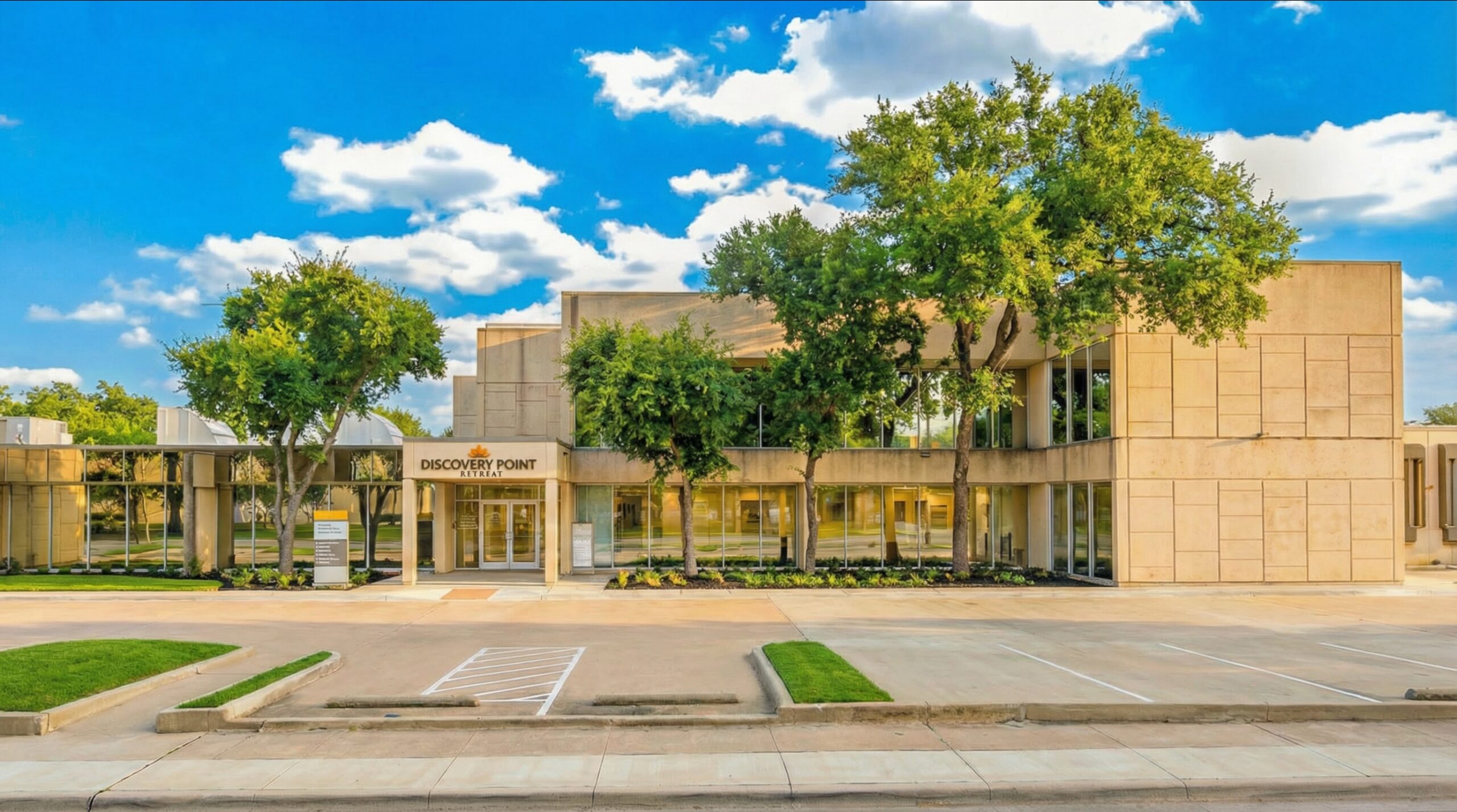Wide exterior view of Discovery Point Retreat Dallas showing the multi-level facility, landscaped grounds, trees, and parking area