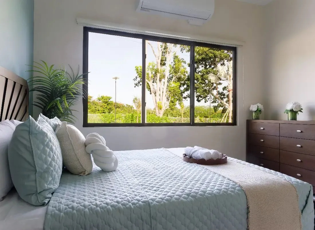 Bedroom with soft bedding and window view of trees.