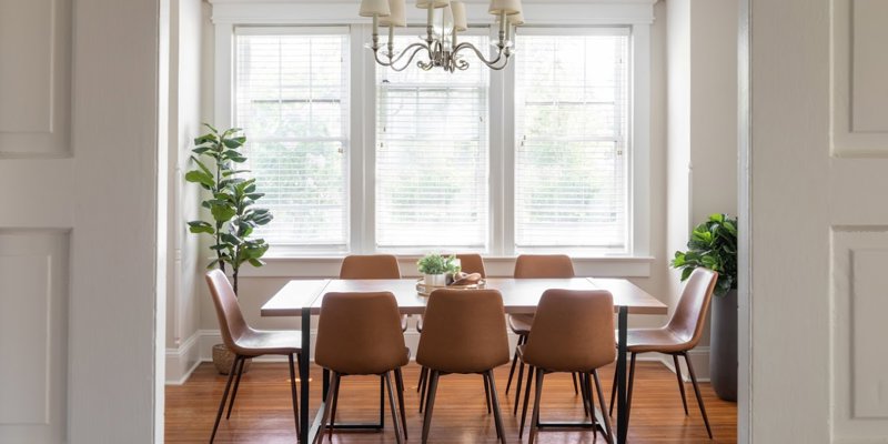 An elegant dining room with a large table, stylish chairs, and natural light. Greenery adds warmth, perfect for shared meals.