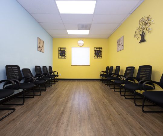 Long room with two rows of black chairs and yellow walls