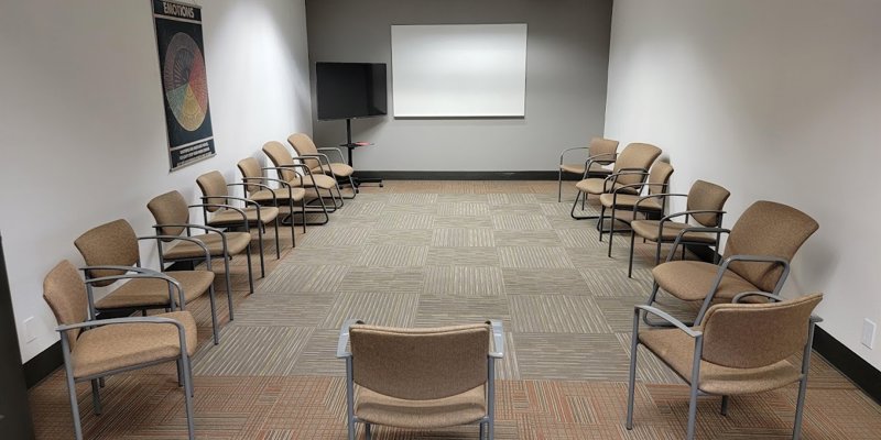 A spacious, well-lit group therapy room with comfortable chairs arranged in a circle. The neutral tones create a calm, focused environment.