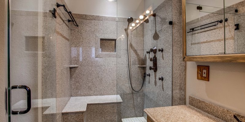  A luxurious bathroom with a spacious, glass-enclosed shower featuring granite walls, built-in seating, and modern fixtures, offering a spa-like experience.