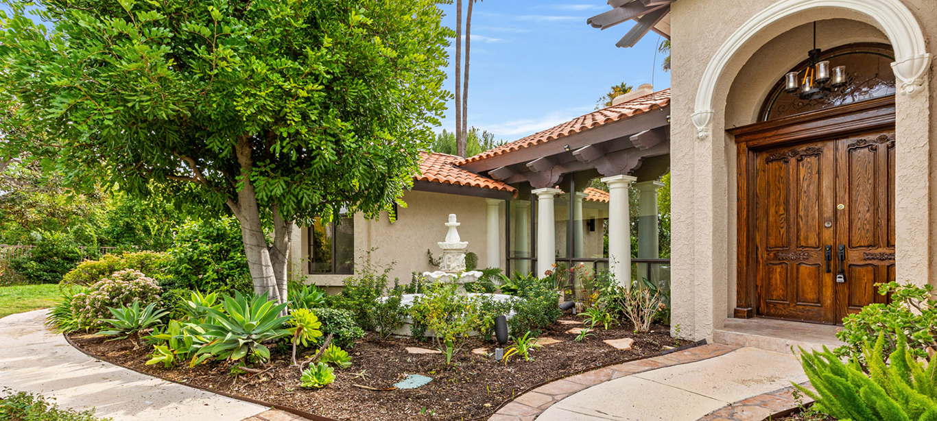 Lush garden walkway leading to a wooden front door and fountain.
