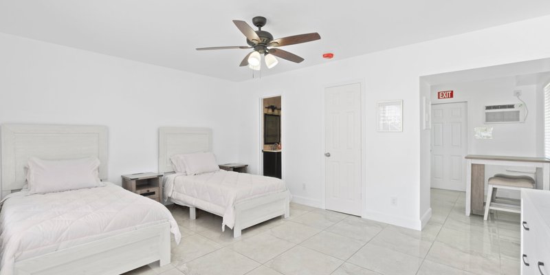 A bright, clean room with two cozy beds, minimalist decor, and ample natural light offers a fresh and welcoming space for rest and relaxation.