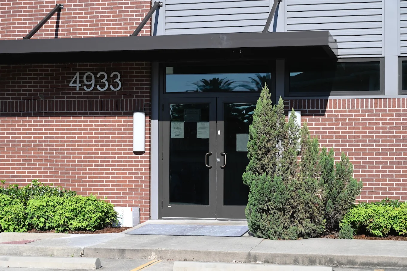 Main entrance at 4933 featuring double doors, brick exterior, covered entryway, and surrounding shrubs