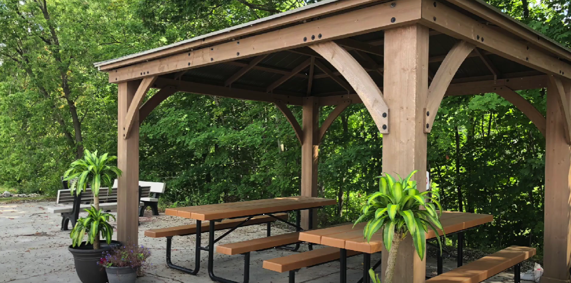 Wooden gazebo with picnic tables and plants in a forested area