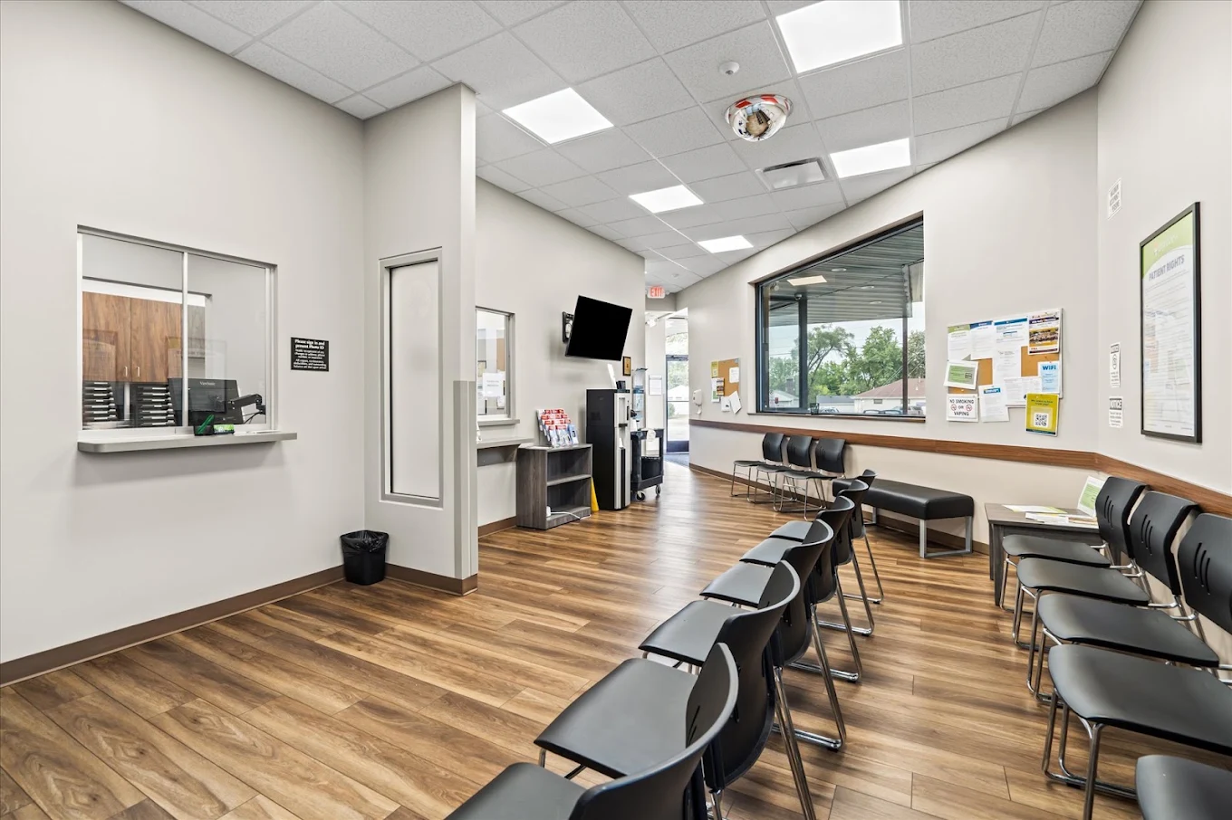 Spacious BrightView Health waiting area with rows of black chairs, reception windows, television, bulletin boards, and large exterior window