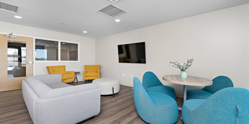 A bright, modern lounge area with cozy blue and yellow armchairs, a soft gray couch, and a round table adorned with fresh flowers for a welcoming touch.