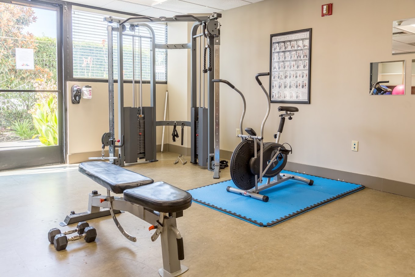 A small gym with exercise machines, a bench, and a training poster