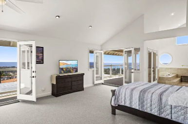A bright bedroom with large windows, a bed, and a view of the ocean.