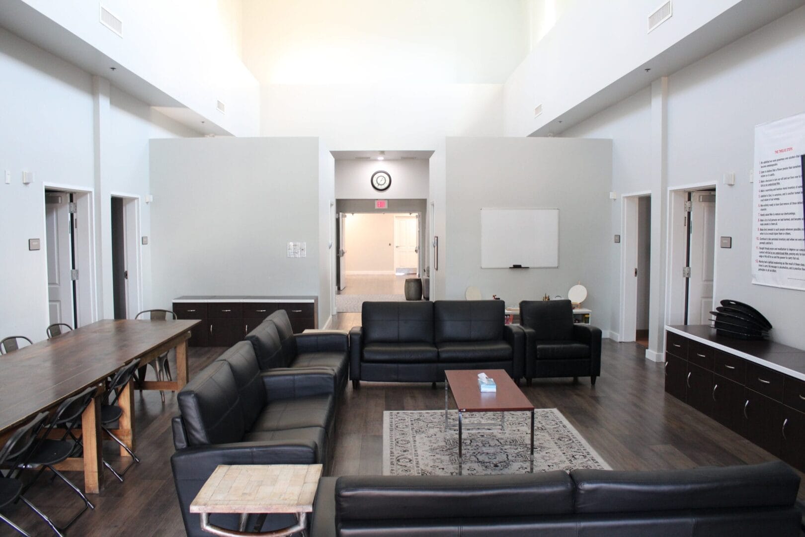 Common area with black couches, dining table and a whiteboard,.