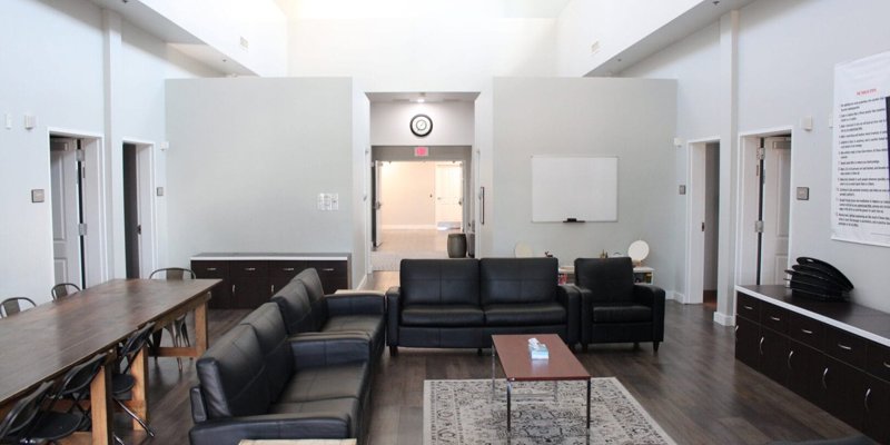 A spacious common area with black leather couches, a wooden dining table, and a whiteboard, offering a comfortable and collaborative environment.