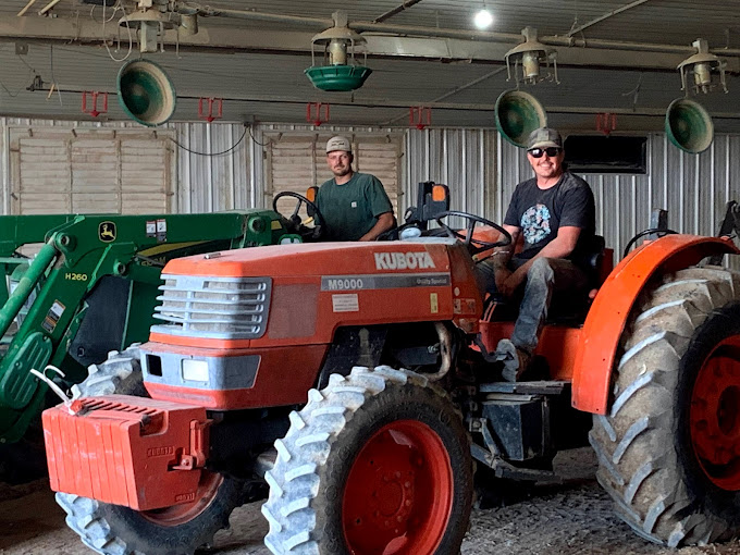 Smiling man on a tractor indoors with another person in the background.