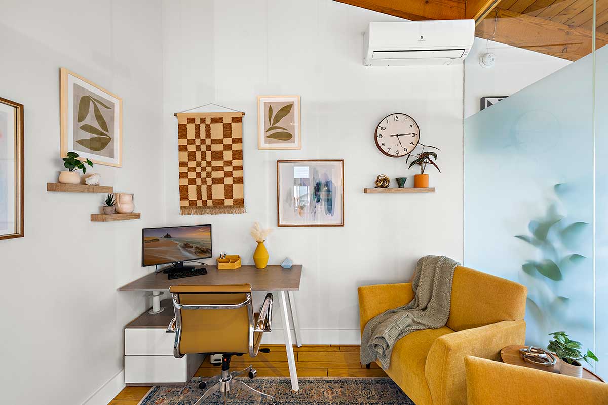 Comfortable consultation room with desk, office chair, mustard armchair, wall art, plants, and frosted glass partition