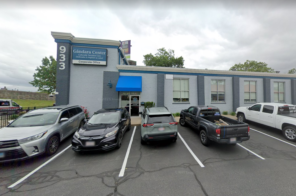 Gray brick building with blue awning and cars parked in front