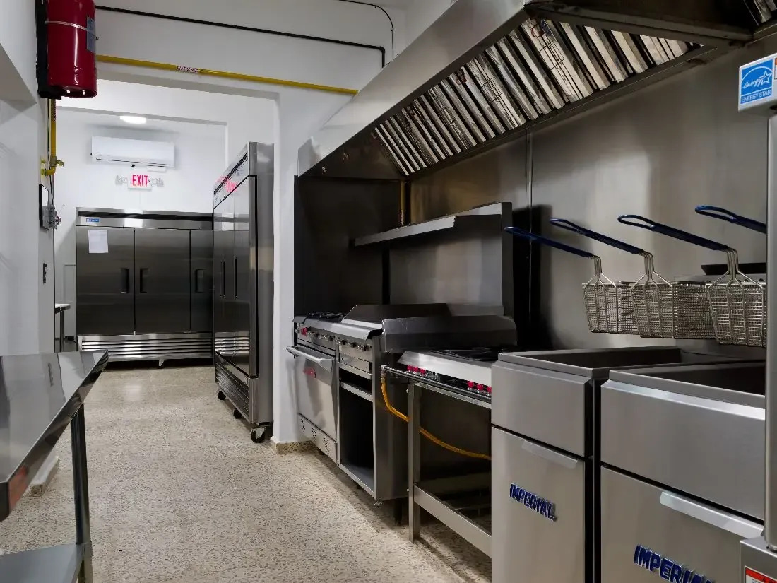 Stainless steel commercial kitchen with stoves and storage.