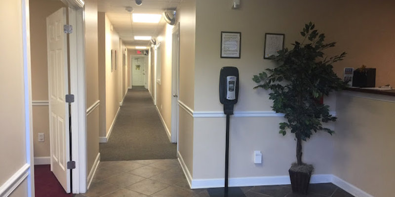 A clean, well-lit hallway with tiled floors and wall-mounted sanitizer, creating a welcoming and organized environment. A potted plant adds warmth.