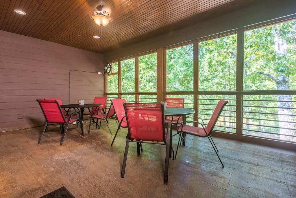Screened porch with red chairs and a forest view