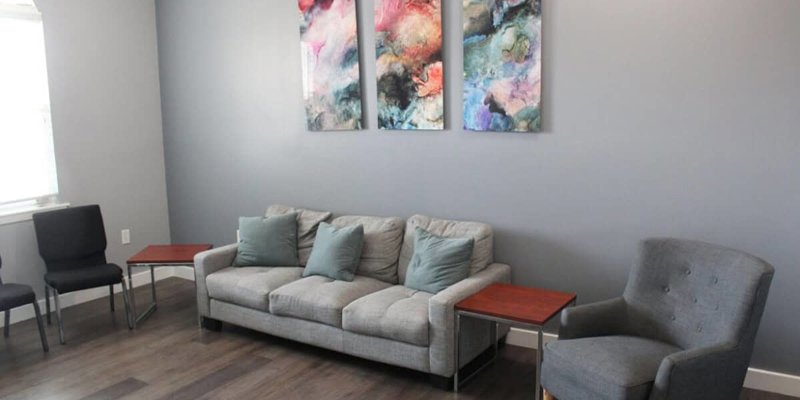 A cozy seating area with a soft gray couch, accent pillows, and a modern armchair, complemented by colorful abstract wall art for a relaxing vibe.