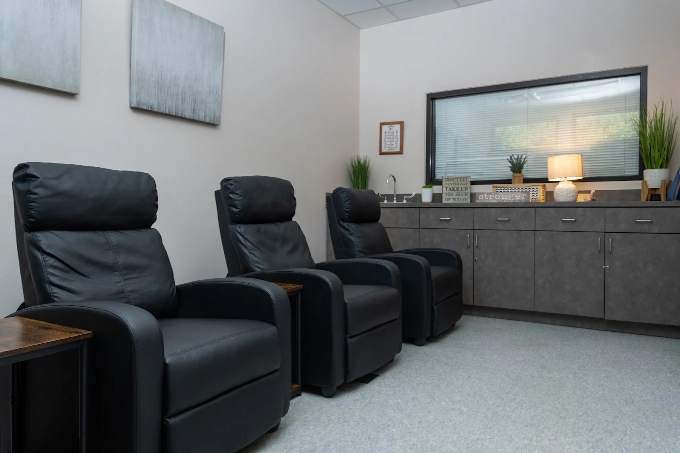 Treatment room with three black reclining chairs, storage cabinets, plants, and soft lighting