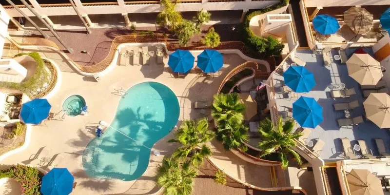  Aerial view of a vibrant outdoor pool area with bright blue umbrellas, comfortable lounge chairs, and lush greenery for a relaxing experience.