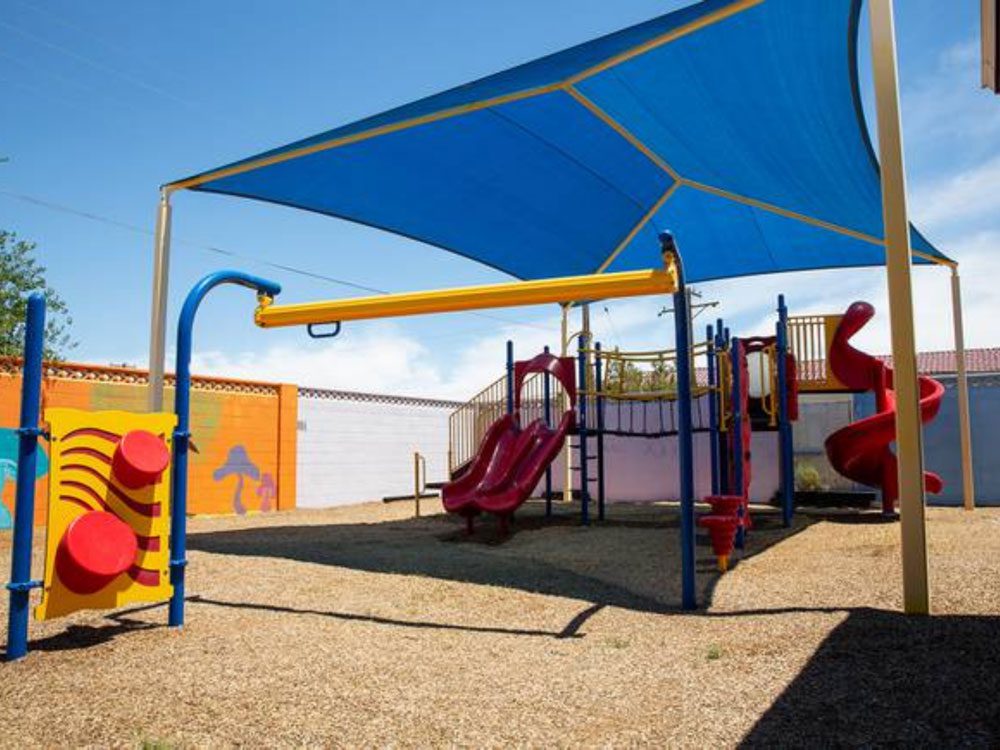 Outdoor playground with slides and climbing structures under canopy