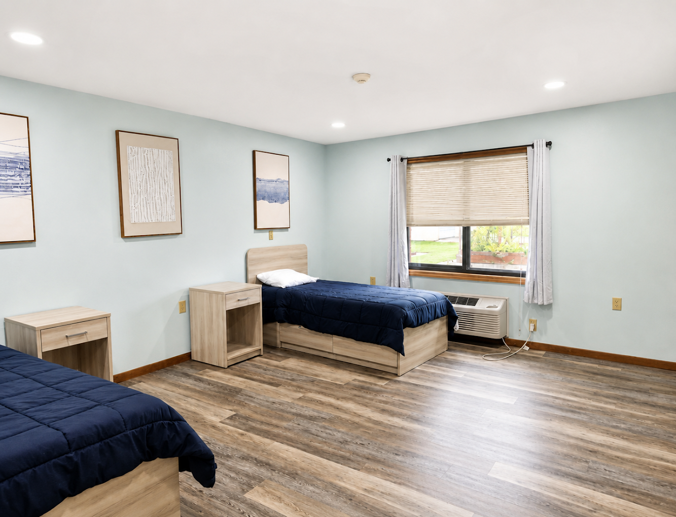 Shared bedroom with two beds, windows, and wood flooring