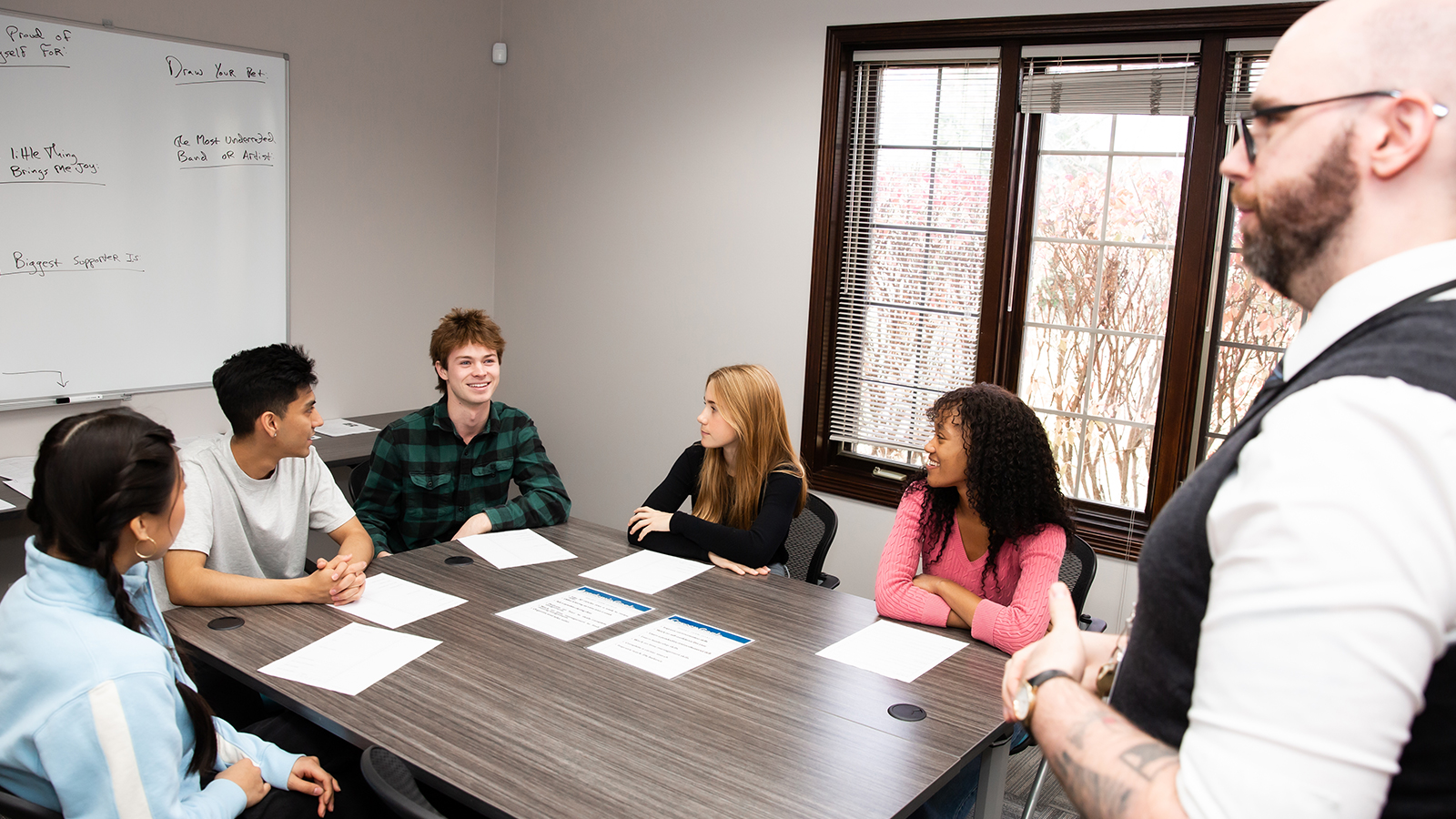 Young adults sitting at a table with a facilitator standing.