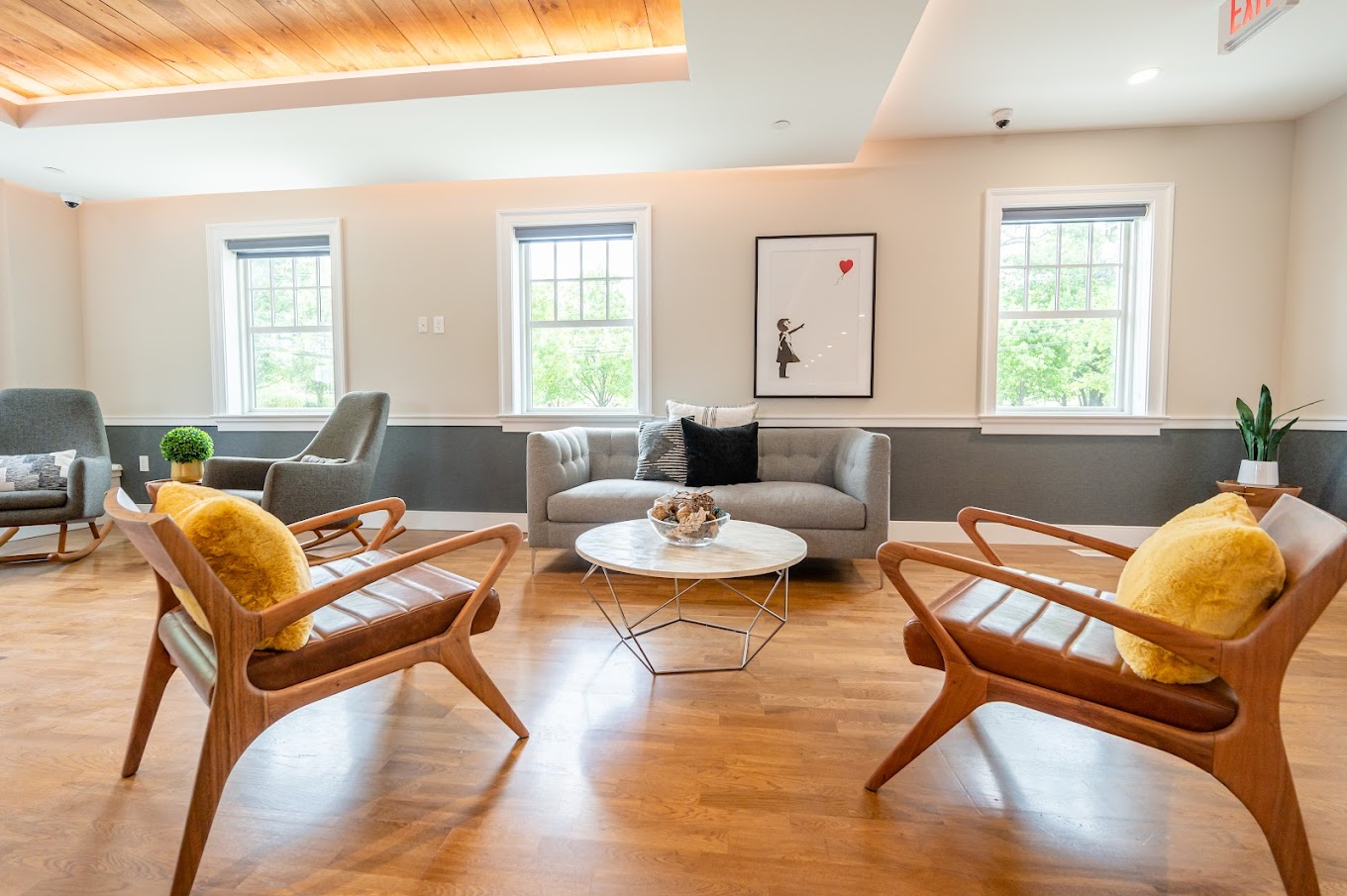 A stylish and comfortable lounge featuring mid-century modern chairs, a small round coffee table, and framed artwork, with large windows providing natural light.