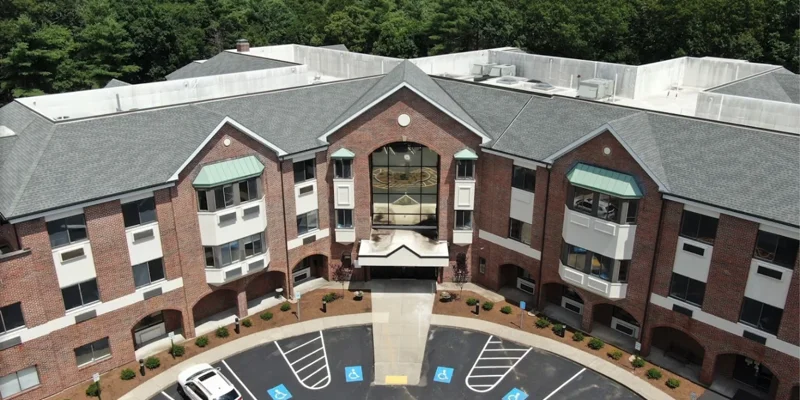 Aerial view of a modern, well-maintained brick building surrounded by greenery, featuring accessible parking and a welcoming entrance.