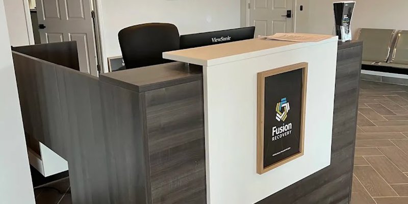  A modern, professional reception desk at Fusion Recovery, featuring sleek wood accents, clean lines, and a warm, welcoming atmosphere.