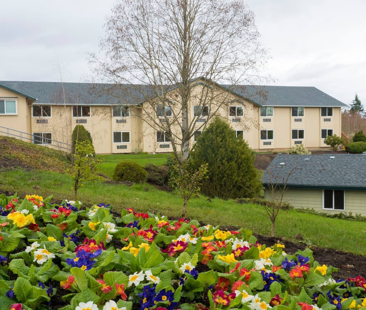 Facility exterior sits behind a garden and a smaller building.