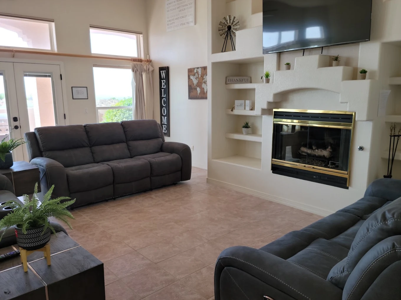 Comfortable living room with reclining sofas, fireplace, television, built-in shelving, and large windows