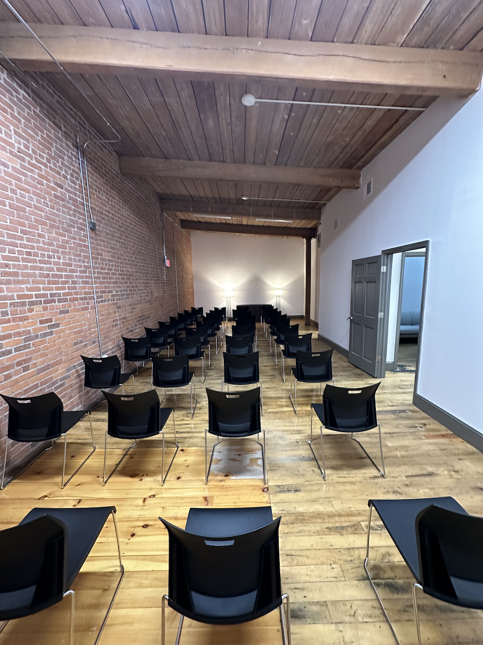 Lecture-style room with rows of black chairs and exposed brick walls