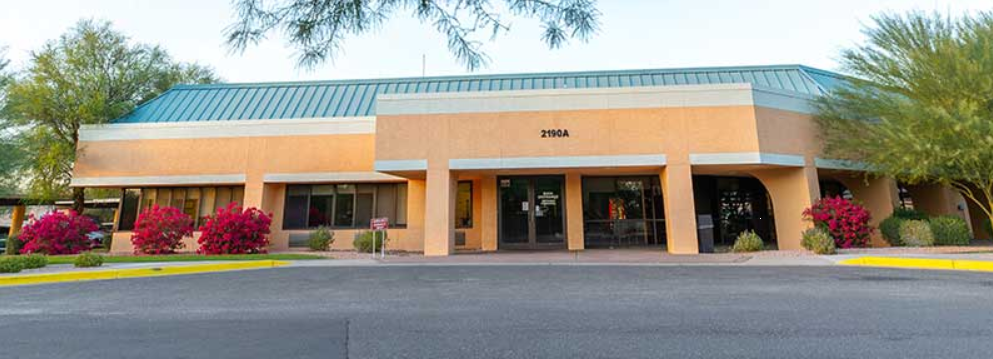 Single-story tan building with teal roof and flowering bushes
