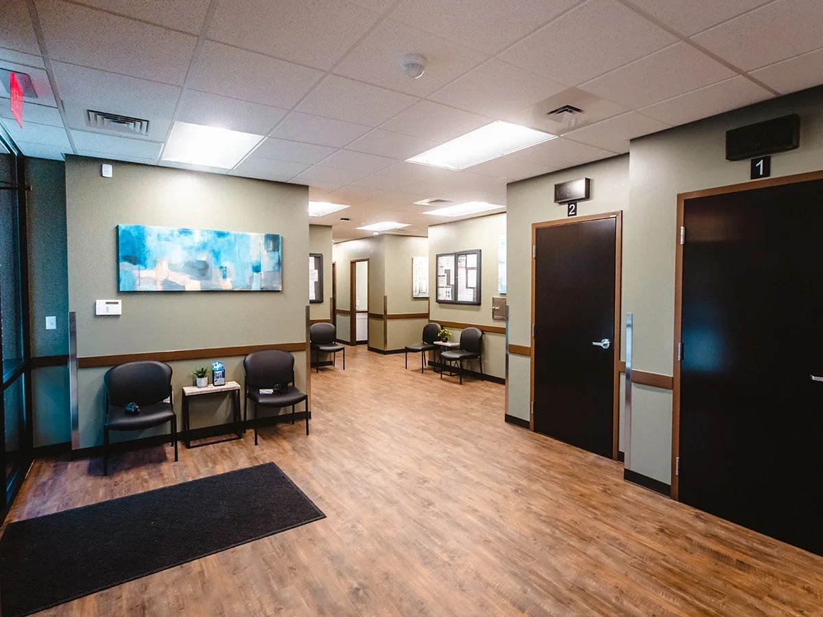 Clean hallway with chairs along wall, numbered doors, and wood flooring