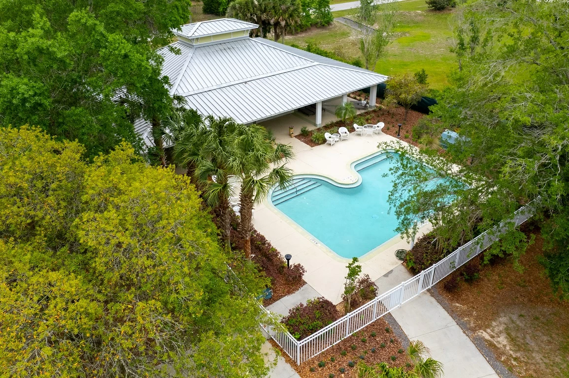 Outdoor swimming pool surrounded by lounge seating, palm trees, and fenced patio area at recovery center