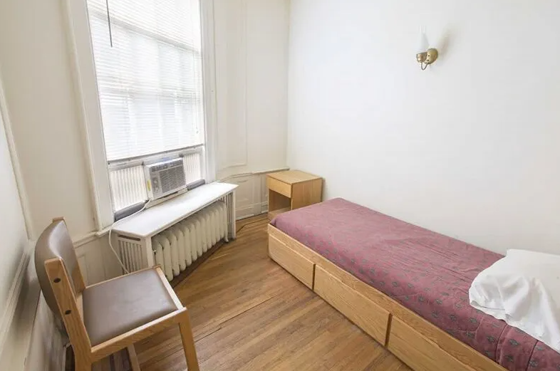 Bright single bedroom with wooden furniture and window air conditioner